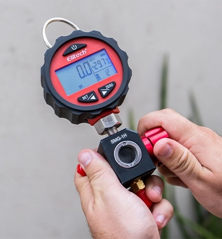 Mãos segurando um manifold digital da Elitech Brasil na cor vermelha.