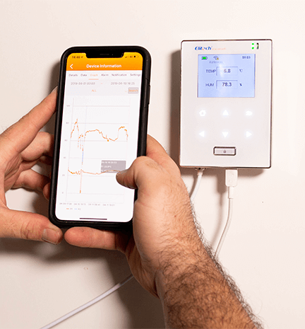 Uma mão segurando um celular, mostrando o elitech software, que oferece dados na tela do aparelho de temperatura e umidade